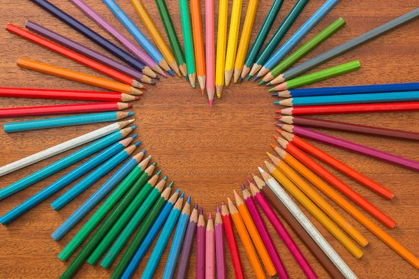 Lápices de colores formados en forma de corazón sobre una mesa de madera —  Fotos de Stock