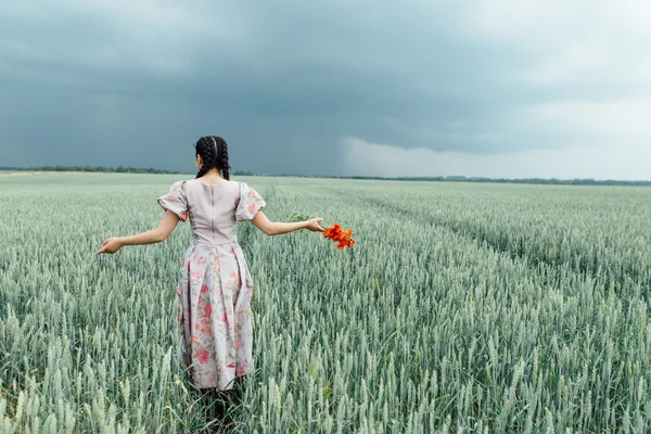 Ein junges hübsches Mädchen läuft auf dem Feld mit grünem Weizen — Stockfoto