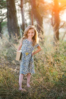 Çimenlerin üzerinde oturan ve bir kitap okuma sevimli küçük kız 