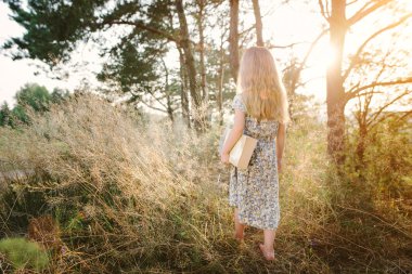 Çimenlerin üzerinde oturan ve bir kitap okuma sevimli küçük kız 