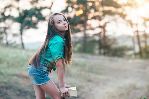 Linda niña sentada en la hierba y leyendo un libro en el —  Fotos de Stock