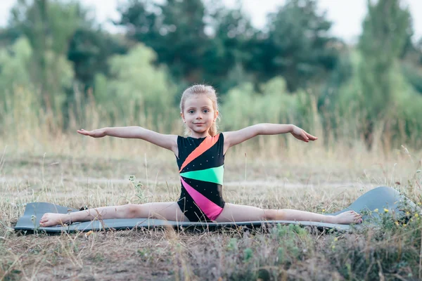 Petite fille mignonne gymnaste assis sur une fente sur des nattes dans les bois — Photo