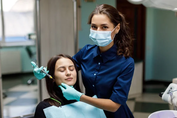 Young woman sits in the dentist\'s chair and the dentist carefully examines the patient\'s teeth. The dentist consults a patient sitting in a chair at the clinic