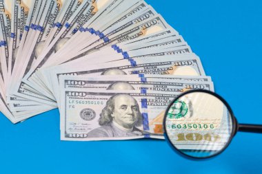 Mavi arka planda dolar banknotları ve büyüteç