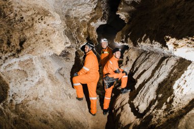 Üç adam, güçlü vücutlu, mağarayı keşfedin. Mağaradan geçmek için özel giyinmiş adamlar durup haritaya baktılar..