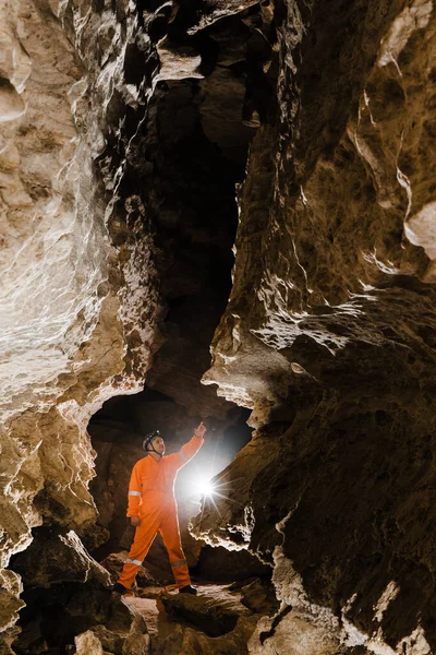 Man walking and exploring dark cave with light headlamp underground.