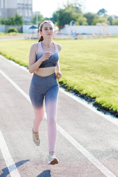 Happy track running girl runner getting ready for cardio training run on lane athletic tracks in stadium campus.