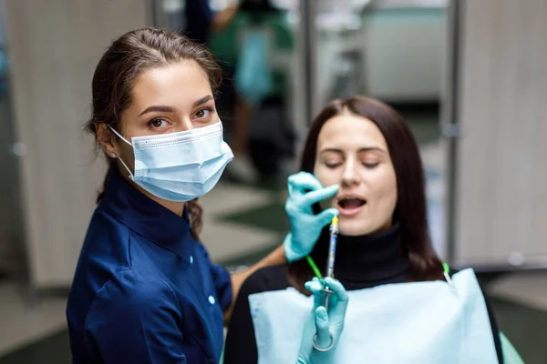 Young woman sits in the dentist\'s chair and the dentist carefully examines the patient\'s teeth. The dentist consults a patient sitting in a chair at the clinic