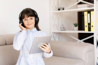 Çocuklar, eğitim ve teknoloji konsepti. Kulaklıklı, tablet bilgisayarlı mutlu öğrenci kız.
