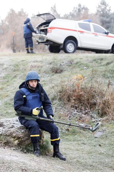 Emergency workers work outdoors. A man in uniform works with a metal detector