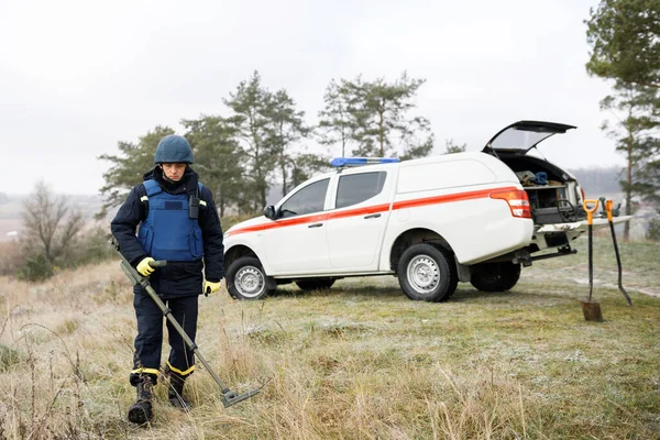 Emergency workers work outdoors. A man in uniform works with a metal detector