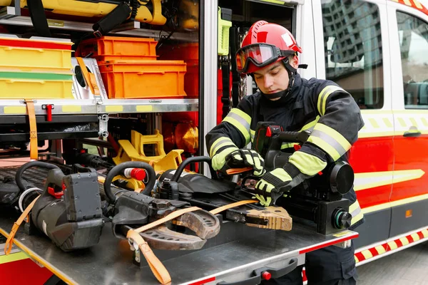 A man of strong physique in uniform and helmet stands by a rescue vehicle. Man rescuer