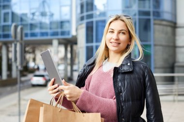 Alışveriş yaptıktan sonra elinde tabletle gezen güzel bir kadın.