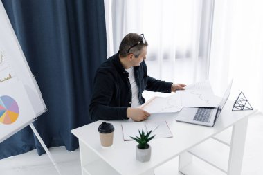 Günlük kıyafetler giymiş bir adam ofiste dizüstü bilgisayarla çalışır ve olumlu duygularını ifade eder. Adam ücra bir yerde çalışıyor.