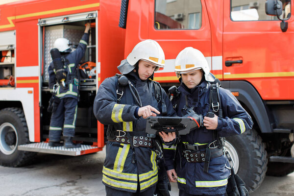 Portrait of two firefighters in fire fighting operation, fireman in protective clothing and helmet using tablet computer in action fighting