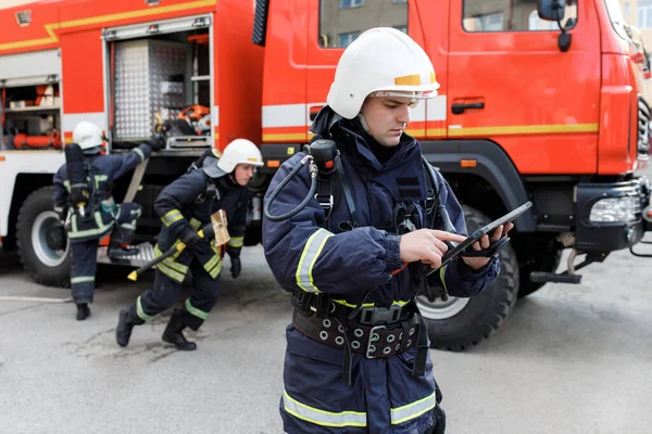 Portrait of firefighter in fire fighting operation, fireman in protective clothing and helmet using tablet computer in action fighting