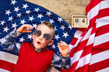 Sevimli ve neşeli bir adam tahta bir arka planda Amerikan bayrağının yanında gözlüklü yatıyor.