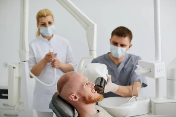 Dentist at work in dental unit with a nurse and a man lying patient. Surgery