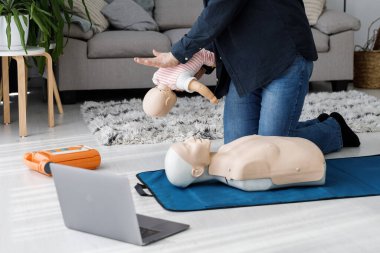 Paramedikler sadece oturma odasında manikine ilk yardım uyguluyor. Eğitmen oyuncak bebek üzerinde suni teneffüs yapıyor.