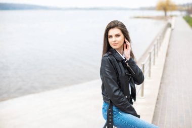 Deri ceket ve kot giyen genç ve güzel bir kız nehirde tek başına vakit geçiriyor..