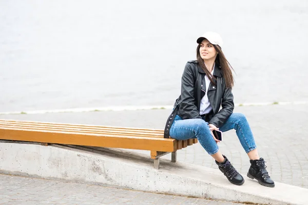 一个穿着皮夹克和牛仔裤的年轻漂亮的姑娘 一个人在河里呆着 — 图库照片