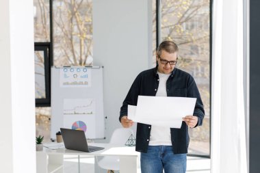 Sıradan giyinmiş bir adam ofiste çalışır ve iş belgelerini karıştırır. Adam ücra bir yerde çalışıyor.