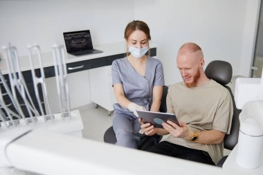 Klinikte orta yaşlı bir adamın yanında duran genç kadın dişçinin portresi.