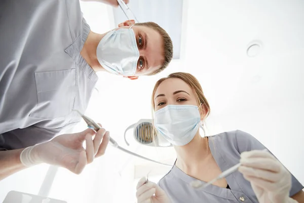 Dentists in masks look at the camera with tools in hands