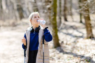 Sarışın sporcu kadın, güneşli bir kış gününde güneşli bir kış gününde, orman yolunda yürüme alıştırması yapıyor.