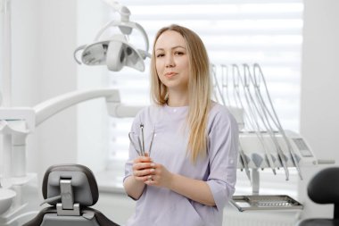 Modern bir diş kliniğinde diş aletlerini tutarken gülümseyen diş hekimi, sağlık ve profesyonel oral hizmetin özünü somutlaştırıyor