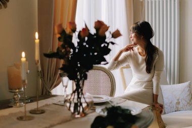 Woman sitting at a table with lit candles and flowers, contemplating during an intimate and elegant dinner setting