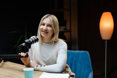 İçerik yaratıcısı, rahat bir ev stüdyosunda ses podcast 'i kaydederken bir mikrofonla meşgul oluyor, mutluluk ve yaratıcılık yayıyor.