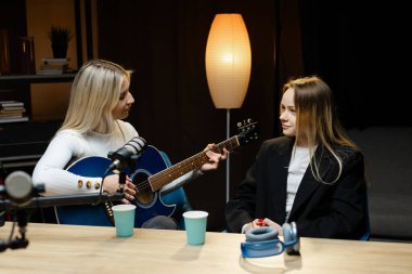 İki bayan müzisyen bir stüdyoda akustik gitar ve profesyonel mikrofonla şarkı çalıyor ve kaydediyor.