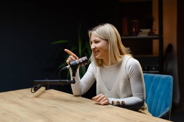 Bir stüdyoda podcast çekerken başarıyı kutlayan genç bir kadın heyecanla ve başarıyla kollarını kaldırıyor.