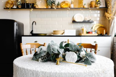 Beyaz dantelli masa örtüsü ve kış çelengi ile zarif mutfak masası tatiller için rahat bir ortam yaratıyor.