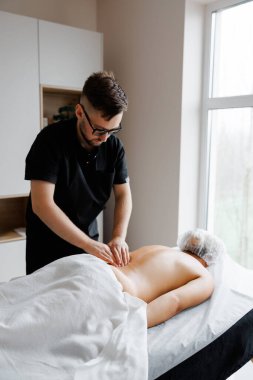 Profesyonel erkek masör müşterisine sırt masajı yapıyor. Parlak bir odada rahatlama ve terapi sağlıyor.