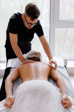 Modern bir spa ya da sağlık kliniğinde kadın müşteriye masaj yapan erkek terapist, rahatlama ve bakımı teşvik ediyor.