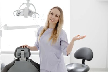 Modern ve parlak diş muayenehanesinde gülümseyen dişçi kadın, ekipmanların yanında duruyor.