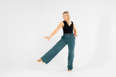 Sarışın bir kadının bütün vücut portresi beyaz bir arka planda elleri bağlı ve bacakları ayrık dans ediyor.