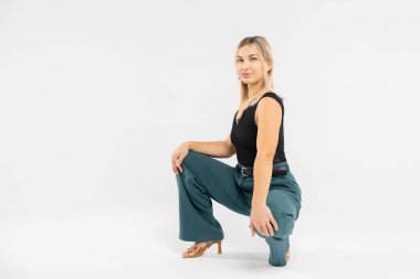 Zarif bir ofis elbisesi içindeki genç sarışın, stüdyo ortamında çömelmiş, kendine güveni ve tarzı olan