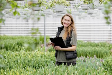 Kitapları olan genç bir bayan işçi lalelerle serada duruyor..