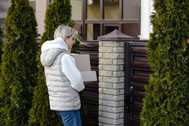 Genç bir kadın, güneşli bir bahar gününün tadını çıkarırken, meskun bir mahallede kaldırımda yürürken iki karton kutu taşıyor.