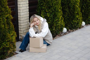 Genç bir kadın evinin önünde elinde iki karton kutuyla oturmuş online alışveriş deneyiminin tadını çıkarıyor.