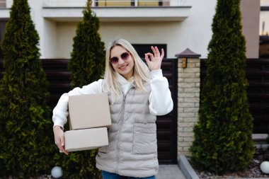 Karton kutular taşıyan ve evin önünde duran gülümseyen teslimatçı kadın.