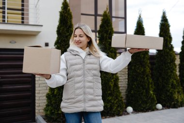 İki karton kutu taşıyan teslimatçı kadın, ev teslimatını yönetiyor ve verimlilik ve güvenilirlikle e-ticaret nakliyatı yapıyor.