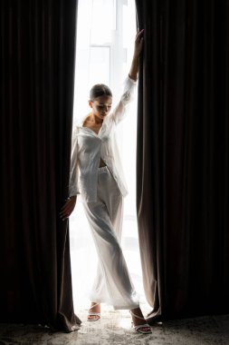 Gelin beyaz ipek pijama giyip, tüylü kelepçelerle düğün günü iki siyah perde arasında perde açıyor.
