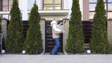 Evin önünde karton kutular taşıyan gülümseyen teslimatçı kadın.