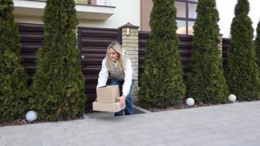 Müşteri akıllı telefon kullanıyor. Eve teslim için bekliyor. Evin yanında karton kutular var.