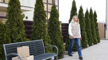 Evin önünde karton kutular taşıyan gülümseyen kadın.