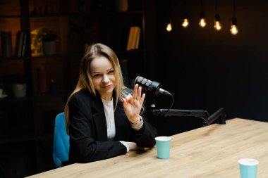 Genç bayan radyo sunucusu bir mikrofona konuşurken ve bir stüdyoda podcast yaparken tamam işareti yapıyor.